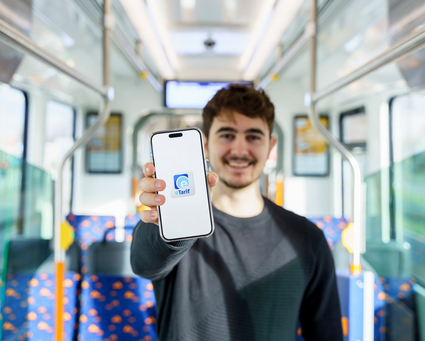 Symbolbild eTarif: Ein Mann steht in einer Straßenbahn der rnv und hält ein Smartphone mit dem Logo der rnv-eTarif-App in die Kamera.