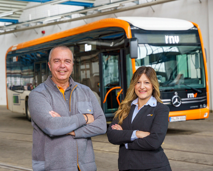 Eine Busfahrerin und ein Busfahrer der Rhein-Neckar-Verkehr GmbH (rnv) in Dienstkleidung vor einem Bus des Typs eCitaro in der Fahrzeughalle.