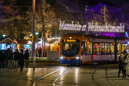 Eine Stadtbahn des Typ Rhein-Neckar-Vario fährt in die Haltestelle Wasserturm ein, mit dem Weihnachtsmarkt Mannheim im Hintergrund.